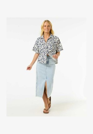 Camicetta floreale a maniche corte in blu navy e bianco, abbinata a una gonna in denim azzurra chiara con spacco frontale e orlo sfrangiato. Indossate sandali marroni.