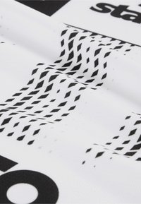 Weißer strukturierter Stoff mit einem schwarzen Netzmuster und grafischen Elementen, einschließlich des Wortes "Stage" in fetten schwarzen Buchstaben.