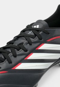 Μαύρο ποδοσφαιρικό παπούτσι με λείο δερμάτινο φινίρισμα, που διαθέτει λευκές και κόκκινες διαγώνιες ρίγες, μαύρα κορδόνια και κεκλιμένο σχέδιο για απόδοση.