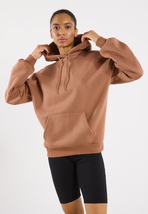 Sudadera marrón con bolsillo frontal y capucha con cordón, combinada con pantalones cortos de ciclismo negros. Tejido suave con un corte relajado y puños acanalados.