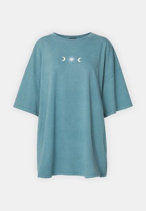 Modrá oversized tričko vyrobené z měkké bavlny. Má krátké rukávy a kulatý výstřih. Grafika na hrudi zahrnuje měsíce a design slunečního výbuchu.