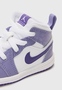 Baskets en cuir blanc et violet clair avec un design montante, lacets blancs et accents violets, arborant un logo sur la languette.