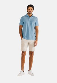 Lichtblauw poloshirt met korte mouwen, gemaakt van een zachte stof; gecombineerd met beige shorts en witte sneakers. Schoon ontwerp met minimale details.