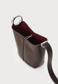 Brun læder håndtaske med en glat tekstur, rektangulær form og et sølvfarvet rundt håndtag. Indvendigt har den en dyb bordeaux-farvet foring.