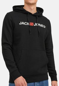 Schwarzer Hoodie mit einer Kängurutasche, der mit "JACK & JONES" Branding in Weiß und Rot versehen ist. Enthält Kordeln und einen weichen, strukturierten Stoff.
