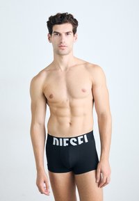 Shorts de boxeur noirs en tissu lisse avec une large ceinture élastique portant le logo "DIESEL" en blanc. Design simple, style ajusté.