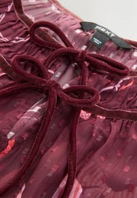 Bordeaux gennemsigtig kjole med tekstureret stof, der har en velour snøre lukning og et ternet mønster langs udskæringen.