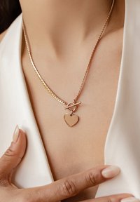 Collier en or rose avec une chaîne torsadée, orné d'un pendentif en forme de cœur et d'un fermoir à bascule. Le pendentif reflète la lumière, ajoutant de l'éclat.