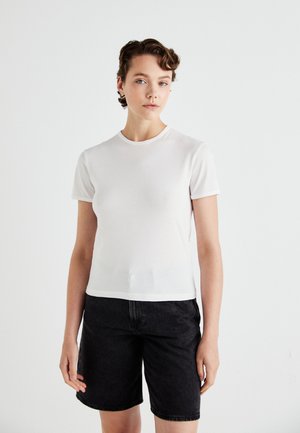 Hvit bomull t-skjorte med korte ermer og rund hals, kombinert med svarte denimshorts. Jevn tekstur, tettsittende design.