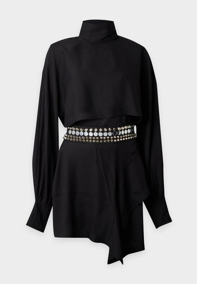 Robe noire à manches longues avec col montant, ourlet asymétrique et large ceinture cloutée avec des clous ronds et pyramidaux argentés.