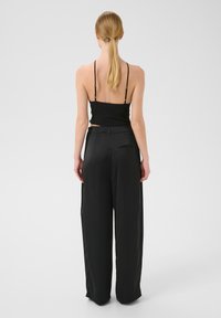 Czarna bluzka na cienkich ramiączkach z wycięciem, zestawiona z czarnymi spodniami o wysokim stanie i szerokich nogawkach. Gładka tekstura i minimalna ilość dodatków.
