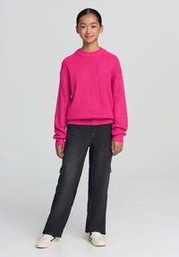 Różowy sweter prążkowany z długimi rękawami, zestawiony z czarnymi spodniami cargo w szerokim kroju z bocznymi kieszeniami oraz białymi sneakersami.