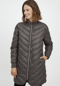 Pilkas pūkuotas paltas su zigzago forma susiūtu raštu, aukštu apykakle, priekiniais užtrauktukais ir šoninėmis kišenėmis; pasižymi blizgia, lygaus paviršiaus tekstūra.