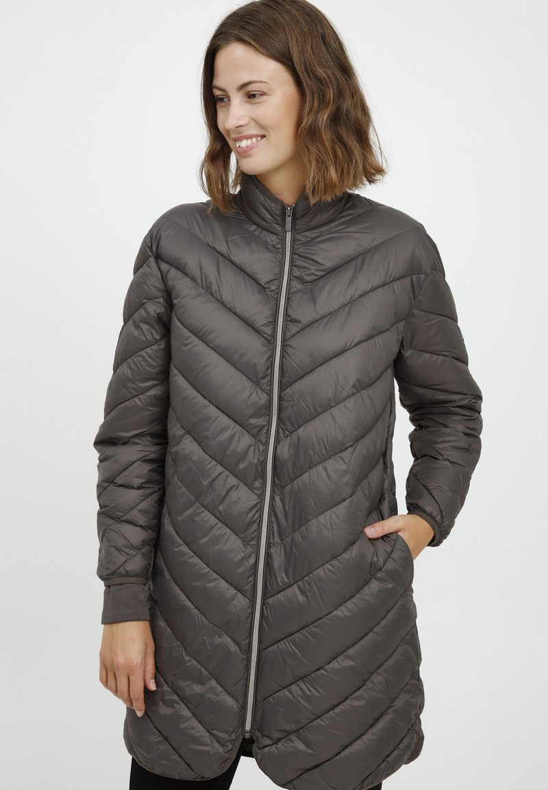 Pilkas pūkuotas paltas su zigzago forma susiūtu raštu, aukštu apykakle, priekiniais užtrauktukais ir šoninėmis kišenėmis; pasižymi blizgia, lygaus paviršiaus tekstūra.