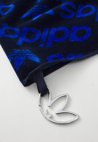Blue velour scarf with repeated "adidas" branding, featuring a silver metal tag shaped like the brand's logo, and a navy ribbon.