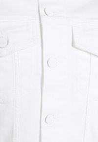 Biała kurtka dżinsowa z zapięciem na guziki, dwoma kieszeniami na piersi i białymi guzikami, wykonana z fakturowanej tkaniny o strukturalnym kroju.