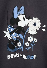 Schwarzer Stoff mit einer Grafik eines Cartoon-Charakters, der eine blaue Schleife und ein gepunktetes Kleid trägt und eine Blume hält. Der Text lautet "Schleifen in Blüte".