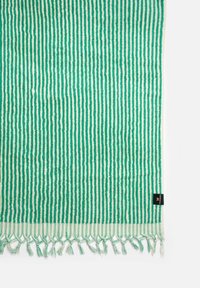 Tessuto a strisce verdi con linee spesse e sottili alternate. Finitura con bordi frangiati e un'etichetta nera, che mette in mostra una superficie testurizzata.
