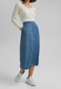 Denim-middellång kjol i ljusblått med rak passform, sidfickor och rå fåll, kombinerad med en krämfärgad ribbad långärmad topp och vita sneakers.