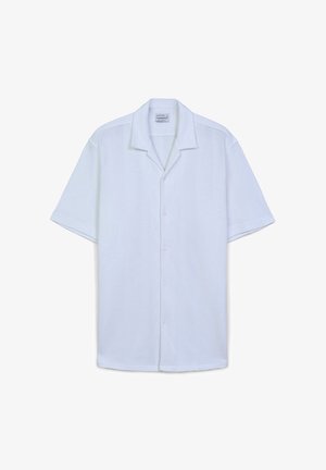 Camicetta bianca a maniche corte realizzata in un tessuto testurizzato, con colletto morbido e chiusura frontale con bottoni; vestibilità leggermente ampia, design semplice.