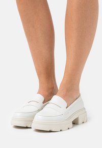 White loafers with a chunky platform, smooth texture, minimalist design, featuring a single decorative seam across the upper section.