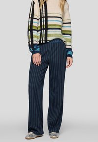 Gestreifter Pullover in Creme, Grün, Blau und Schwarz mit lockerem Schnitt; kombiniert mit marineblauen, weitem Hosen mit vertikalen Streifen und elastischem Bund.