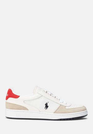 Zapatilla blanca de caña baja con detalles en ante beige, lengüeta roja en el talón, logo de jugador de polo negro en el lateral y cordones blancos sobre una suela plana.