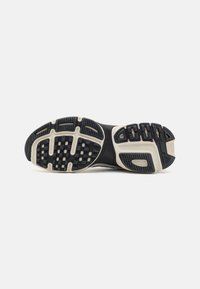 Suola di scarpa sportiva con una superficie in gomma nera, texture antiscivolo. Presenta una intersuola bianca e vari motivi in rilievo per una maggiore trazione.