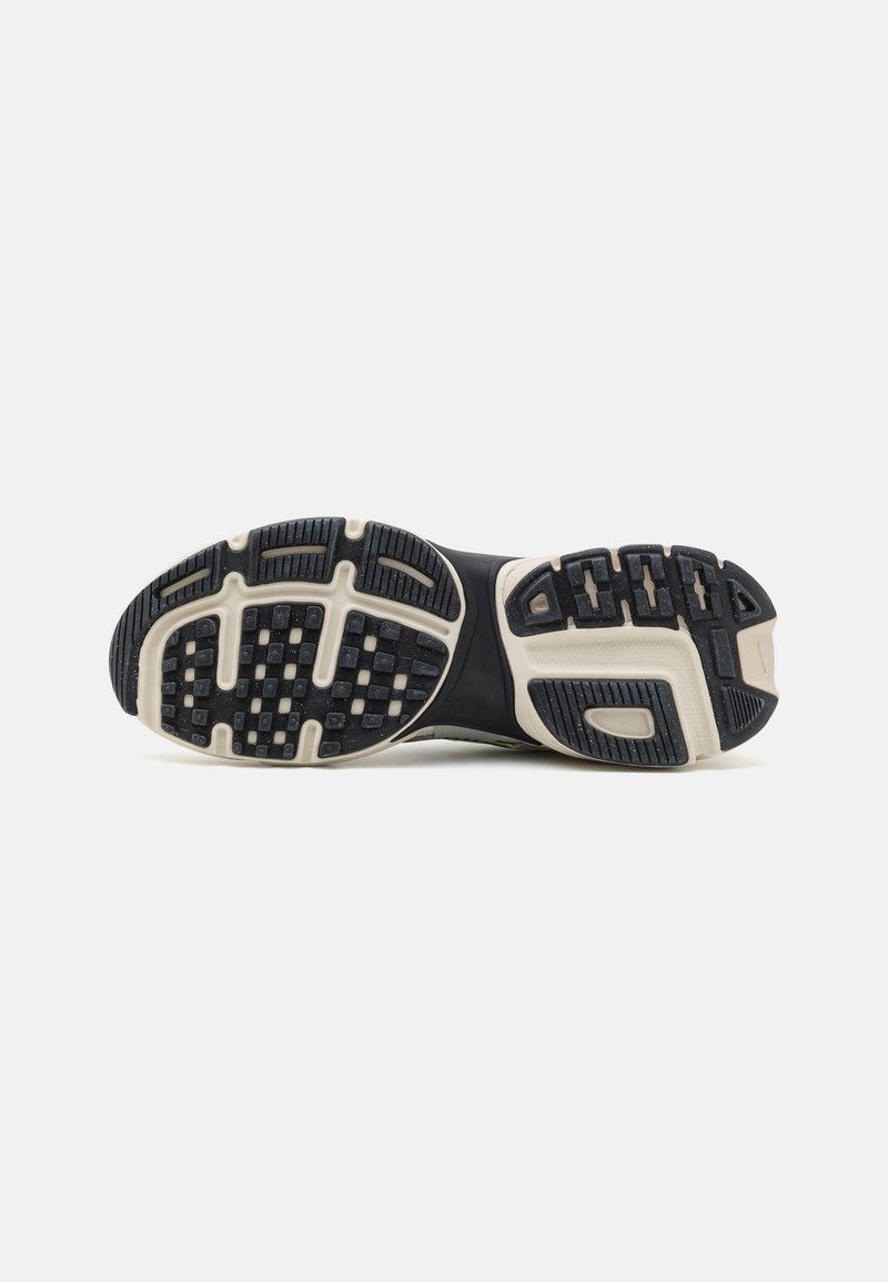 Suela de zapato deportivo con superficie de goma negra, texturizada para un mejor agarre. Presenta una entresuela blanca y varios patrones elevados para la tracción.