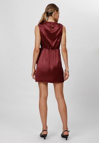 Burgundy satin dress with a fitted waist, sleeveless design, and a back keyhole detail. Styled with black heeled sandals.