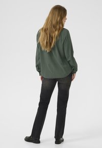 Green long-sleeve button-up shirt, paired with dark jeans and black shoes. Features relaxed fit and smooth fabric texture.