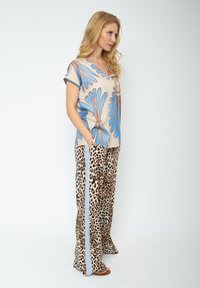 Beżowa bluzka z krótkim rękawem z niebieskim i brązowym wzorem kwiatowym; w połączeniu z spodniami w panterkę z bocznymi pasami. Miękki materiał, luźny krój.