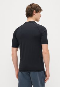 Svart kortärmad träningsskjorta med en mjuk textur och raglanärmar. Har en rund halsringning och kontrasterande sömdetaljer.