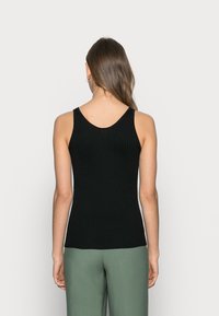 Svart ribbad linne med V-ringning och smala axelremmar, figursydd design, kombinerad med gröna byxor.