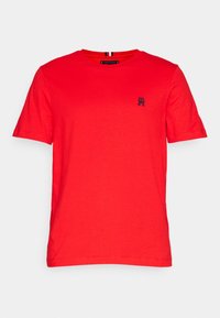 T-shirt en coton rouge avec un col rond, des manches courtes et un petit logo sombre sur la poitrine gauche. Design simple, texture lisse.