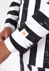 Rukáv obleku s čierno-bielym prúžkovaním a bodkovaným vzorom, s logom na štítku a tromi čiernymi gombíkmi na manžete.