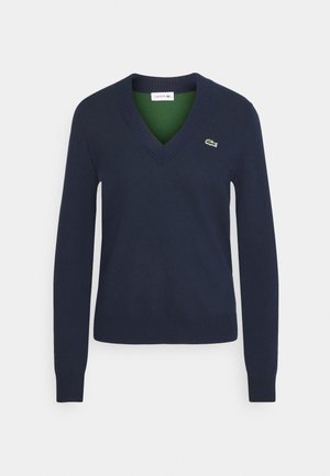 Mørkeblå v-hals sweater lavet af blødt stof, med ribbede manchetter og kant, samt en grøn indre krave og et lille logo på brystet.