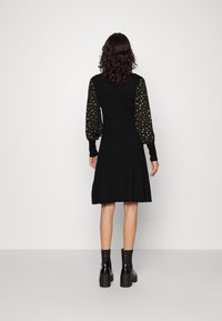 Svart klänning med långa ballongärmar i guldprickar, figurnära liv, utsvängd kjol, ribbade manschetter och en enkel baksida.