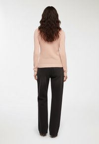 Jasnoróżowy sweter o teksturze, z długimi rękawami, zestawiony z czarnymi spodniami o wysokim stanie i szerokich nogawkach, z tylnymi kieszeniami i czystym wykończeniem.