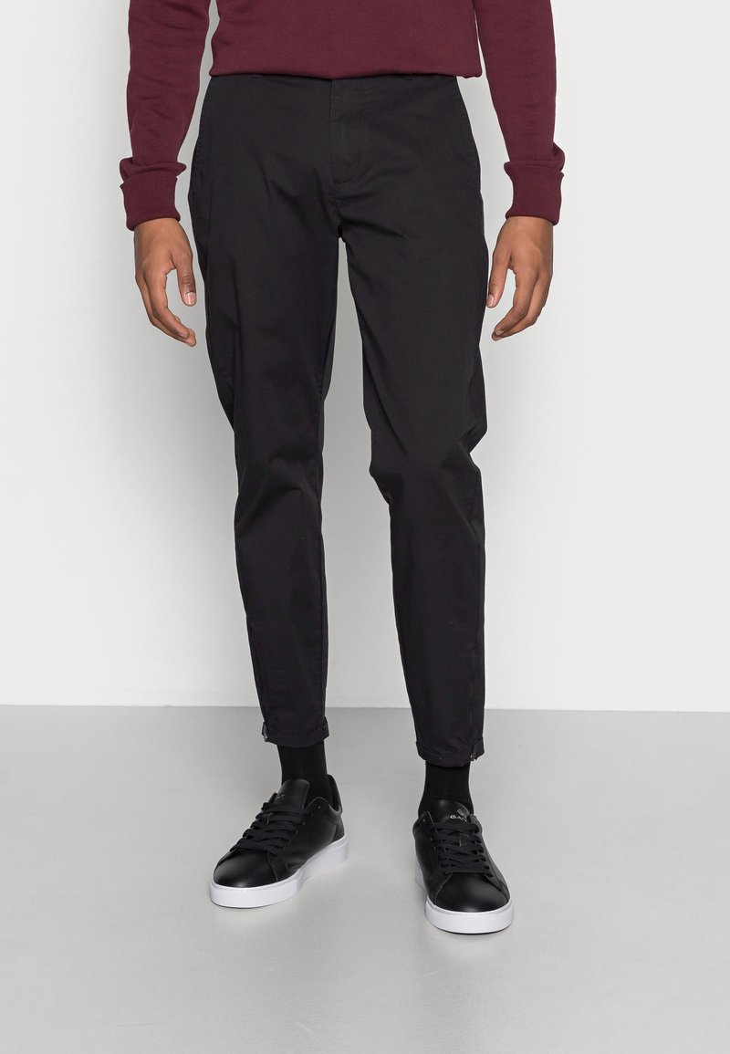 Pantaloni neri a sigaretta realizzati in un mix di cotone, con tasche laterali e zip alle caviglie. Indossati con sneakers nere e una maglia bordeaux.