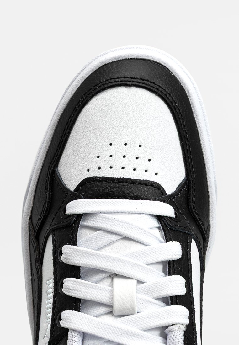 Scarpa sportiva in bianco e nero con tomaia in pelle liscia, punta perforata per traspirabilità e lacci bianchi. Cuciture a contrasto visibili.