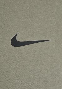 Oliwkowa tkanina sportowa z teksturowaną powierzchnią; na środku widoczny wyraźny czarny logo Nike.