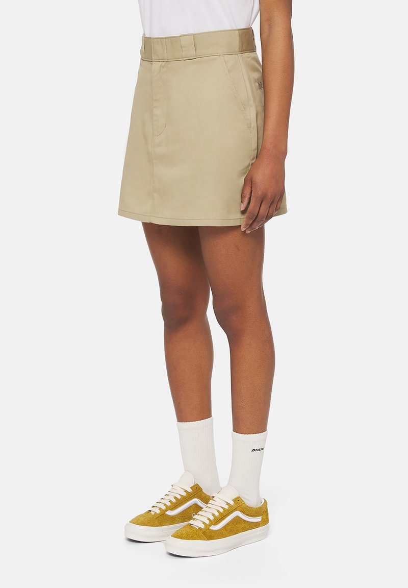 Gonna in cotone beige con vita aderente, tasche laterali e taglio dritto. Abbinata a sneakers in suede giallo e calzini bianchi alla caviglia.
