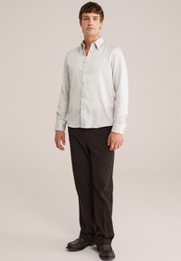 Licht gestreepte overhemd in wit en lichtgrijs, met lange mouwen en een zachte textuur, gecombineerd met donkerbruine op maat gemaakte broek en zwarte schoenen.
