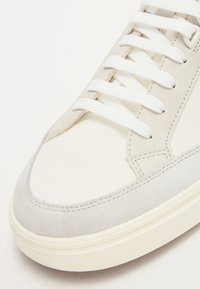 Niedrig geschnittene Sneakers aus einer Mischung aus off-white Canvas und hellgrauem Wildleder, mit weißen Schnürsenkeln und einer strukturierten Gummisohle.
