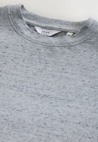 Grijze trui met een gespikkelde textuur, ronde hals en label van NEXT met daarop vermeld dat het een losse pasvorm heeft en maat medium is.