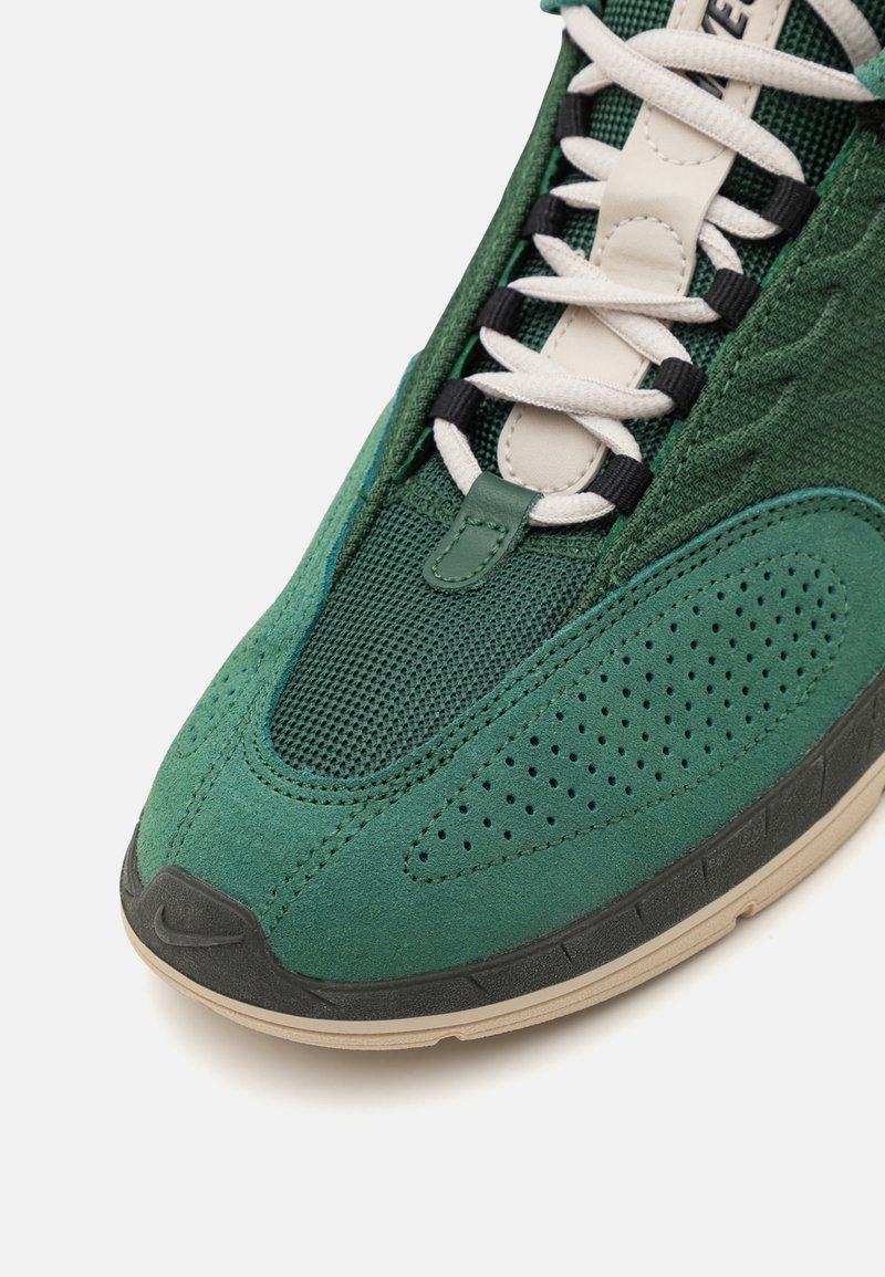 Zapatillas verdes que combinan una mezcla de malla texturizada y ante. Diseñadas con cordones blancos, detalles perforados y una suela de goma negra.