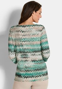 Langarmshirt mit Zickzackmuster in Teal, Weiß und Schwarz, aus leichtem Stoff; verfügt über einen Bootsausschnitt und eine lockere Passform.