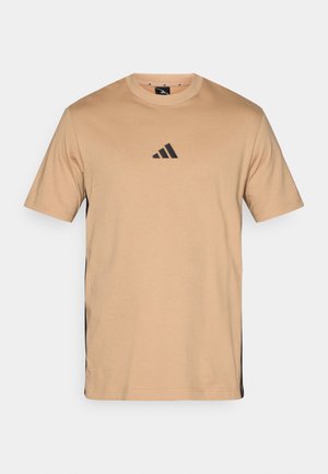 Lys tan t-skjorte med rund hals og korte ermer. Har en svart Adidas-logo på brystet og svarte sideakenter. Laget av bomull.