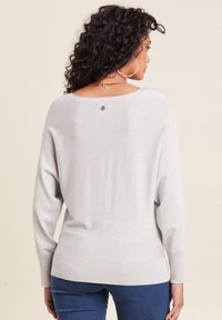 Silberner, locker sitzender Pullover mit weit ausgeschnittenem Rückenteil. Aus einem strukturierten, glitzernden Stoff gefertigt und mit einem kleinen Knopfdetail am Ausschnitt.